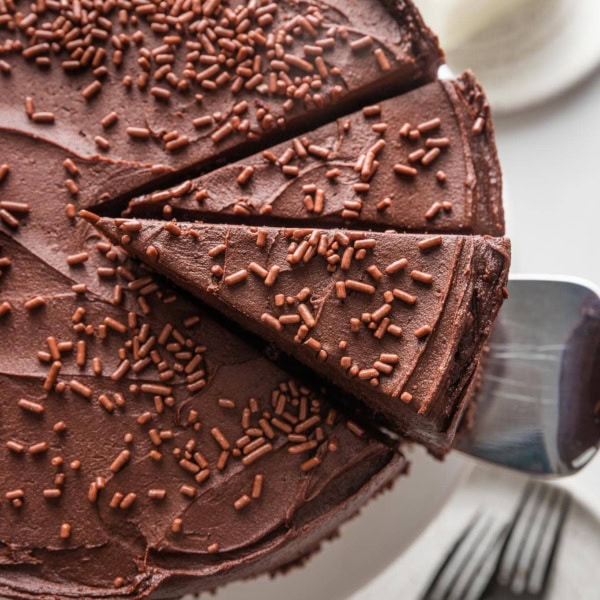 Overhead view of a sliced chocolate buttermilk layer cake with one slice being lifted up and away to serve.