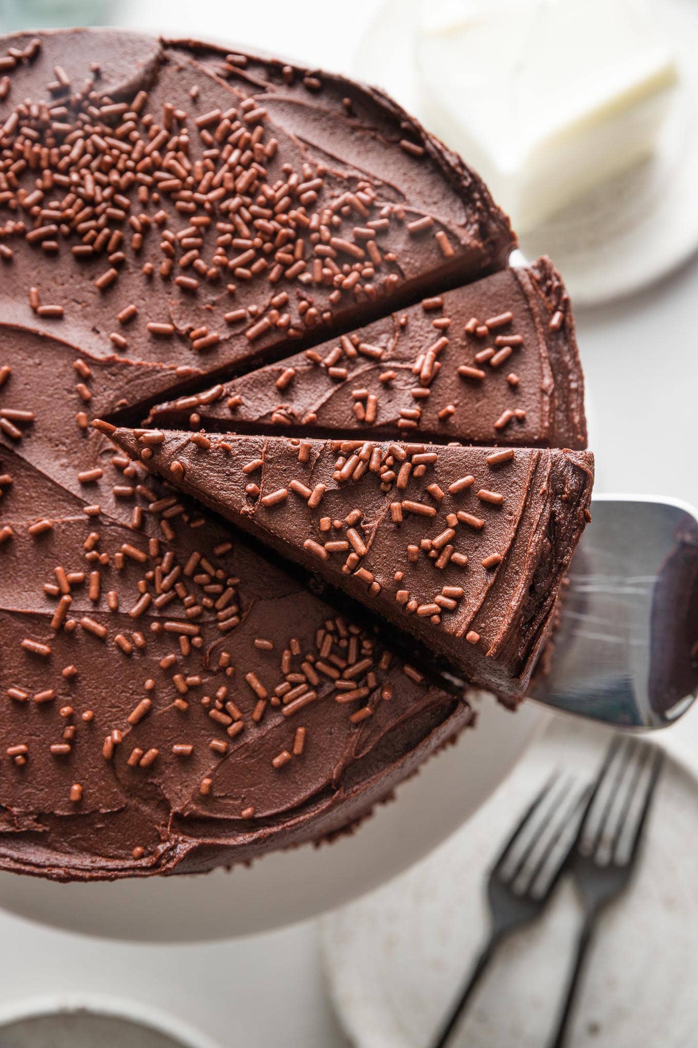 Overhead view of a sliced chocolate buttermilk layer cake with one slice being lifted up and away to serve.