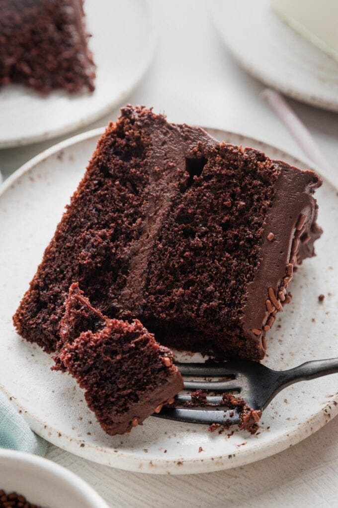 Close up of a slice of a 2 layer chocolate buttermilk cake with chocolate frosting, with a fork lifting out the first bite.