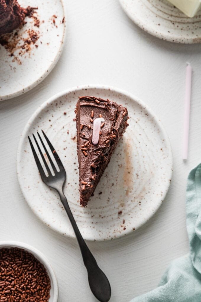 Small dessert plate with a single slice of chocolate buttermilk cake with a candle on top.