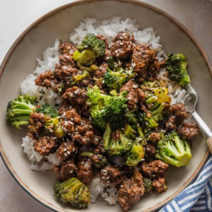 Small low bowl filled with ground beef and broccoli served over rice with a garnish of toasted sesame seeds.
