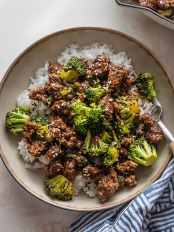 Small low bowl filled with ground beef and broccoli served over rice with a garnish of toasted sesame seeds.
