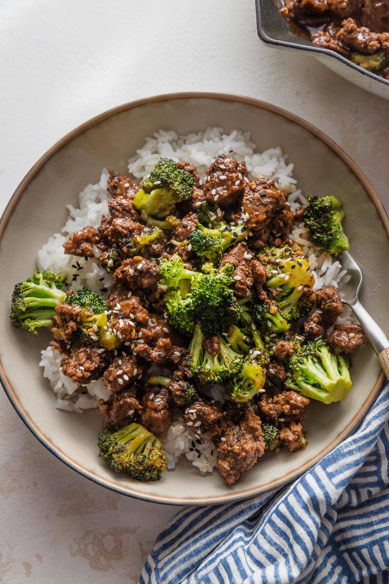 Small low bowl filled with ground beef and broccoli served over rice with a garnish of toasted sesame seeds.
