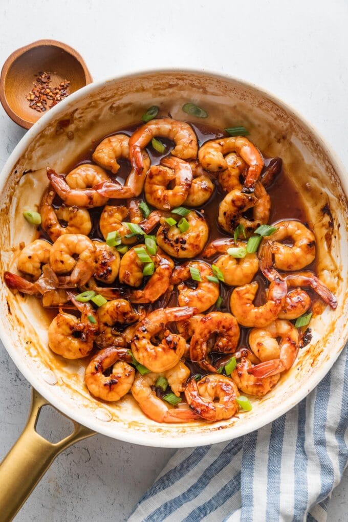 Skillet full of honey garlic shrimp sprinkled with chopped green onions.