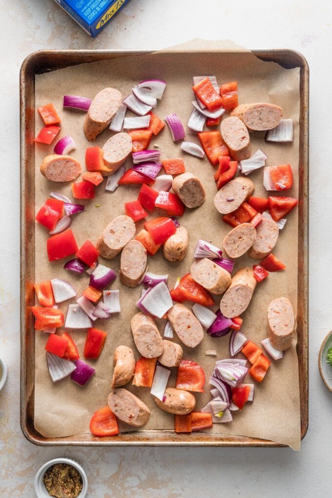 Sheet pan with sliced sausage and veggies, ready to cook.