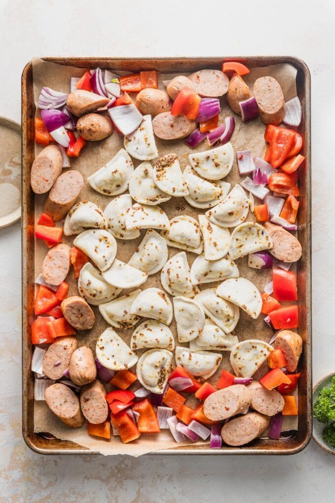 Sheet pan with sausage and veggies pushed to the side and pierogies added to the middle.