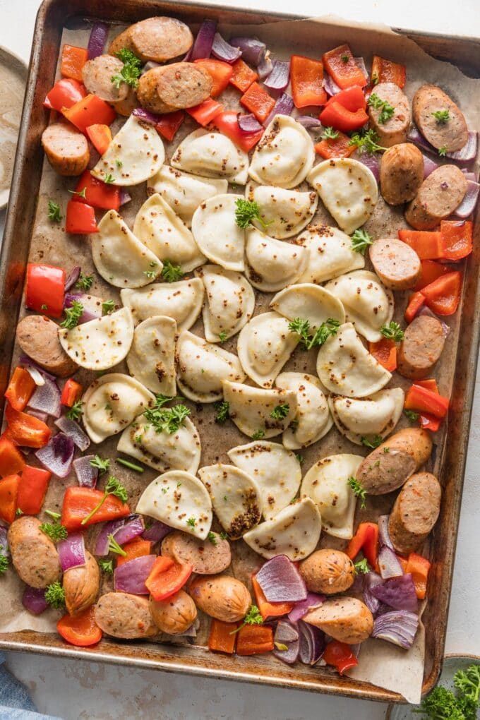Large rimmed sheet pan full of mini pierogies baked with veggies and chicken sausage.