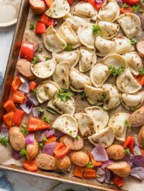 Mini pierogies in a light sauce baked on a sheet pan with peppers and onions.