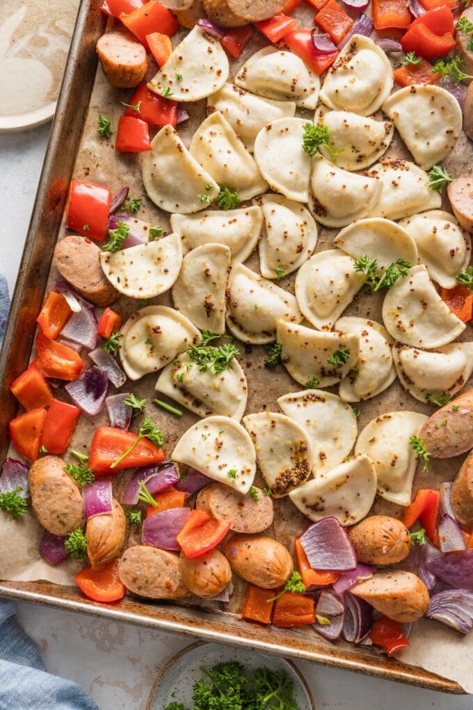 Mini pierogies in a light sauce baked on a sheet pan with peppers and onions.