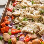 Close up angled view of a mini pierogie sheet pan dinner with sausage, peppers, and onions.