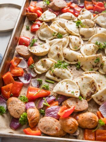 Close up angled view of a mini pierogie sheet pan dinner with sausage, peppers, and onions.