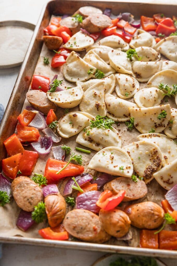 Close up angled view of a mini pierogie sheet pan dinner with sausage, peppers, and onions.