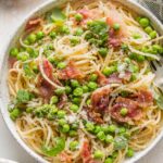 Close up of spaghetti served with a light olive oil sauce, peas, and crisp bacon.