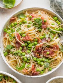Close up of spaghetti served with a light olive oil sauce, peas, and crisp bacon.
