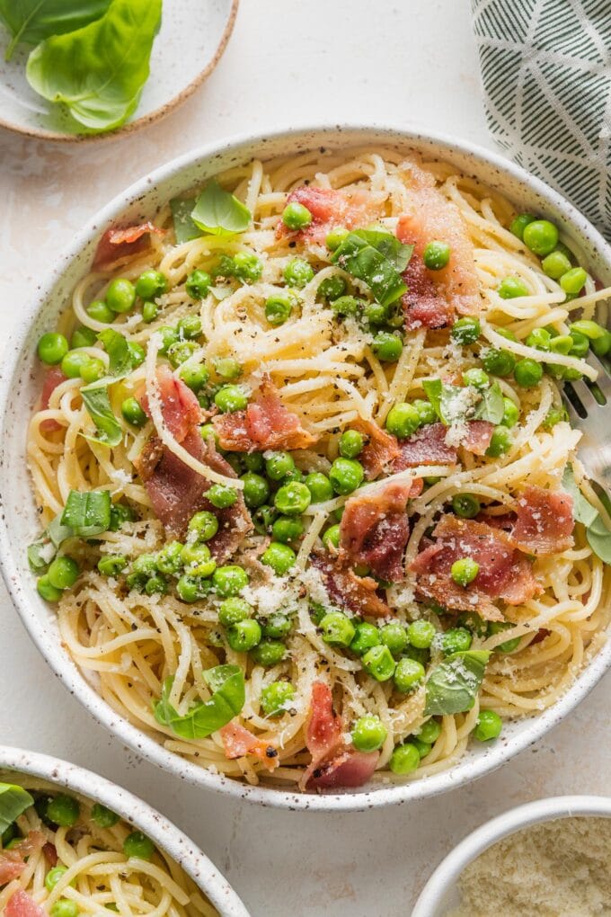 Close up of spaghetti served with a light olive oil sauce, peas, and crisp bacon.
