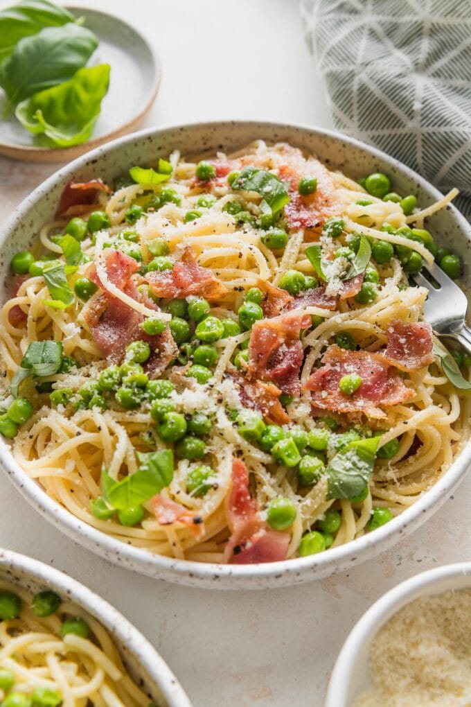 Angled view of a countertop set with two bowls of pasta with bacon and peas.