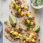White platter holding four carnitas tacos with pineapple jalapeno salsa and diced avocado.