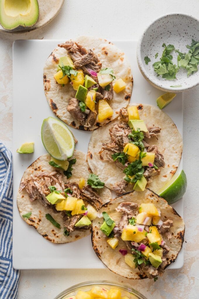 White platter holding four carnitas tacos with pineapple jalapeno salsa and diced avocado.