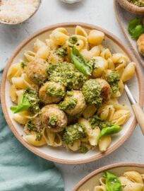 Fork hovering over a bowl of pesto chicken meatballs and pasta.