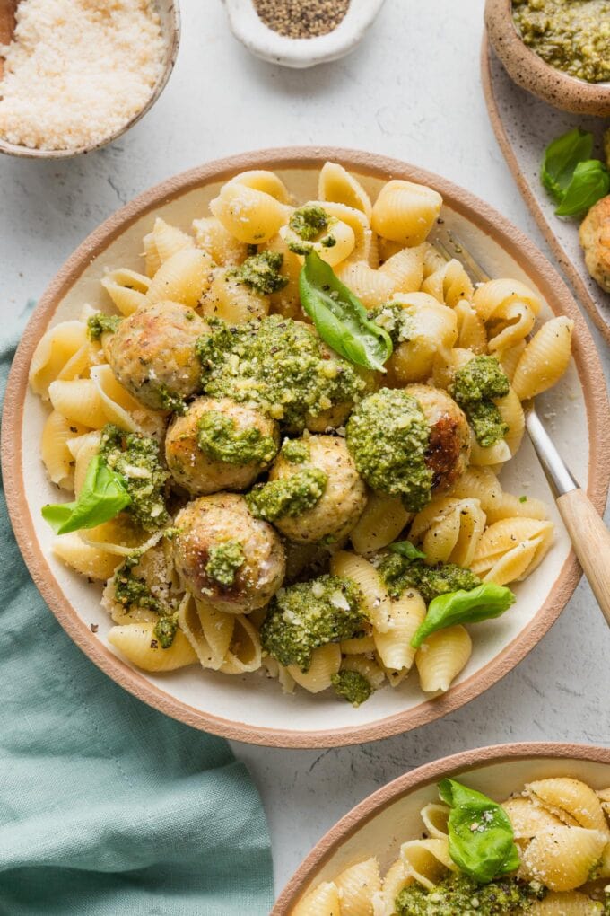 Fork hovering over a bowl of pesto chicken meatballs and pasta.