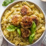 Chicken pesto meatballs served over rotini with Parmesan and fresh basil leaves.
