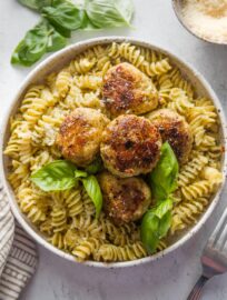 Chicken pesto meatballs served over rotini with Parmesan and fresh basil leaves.
