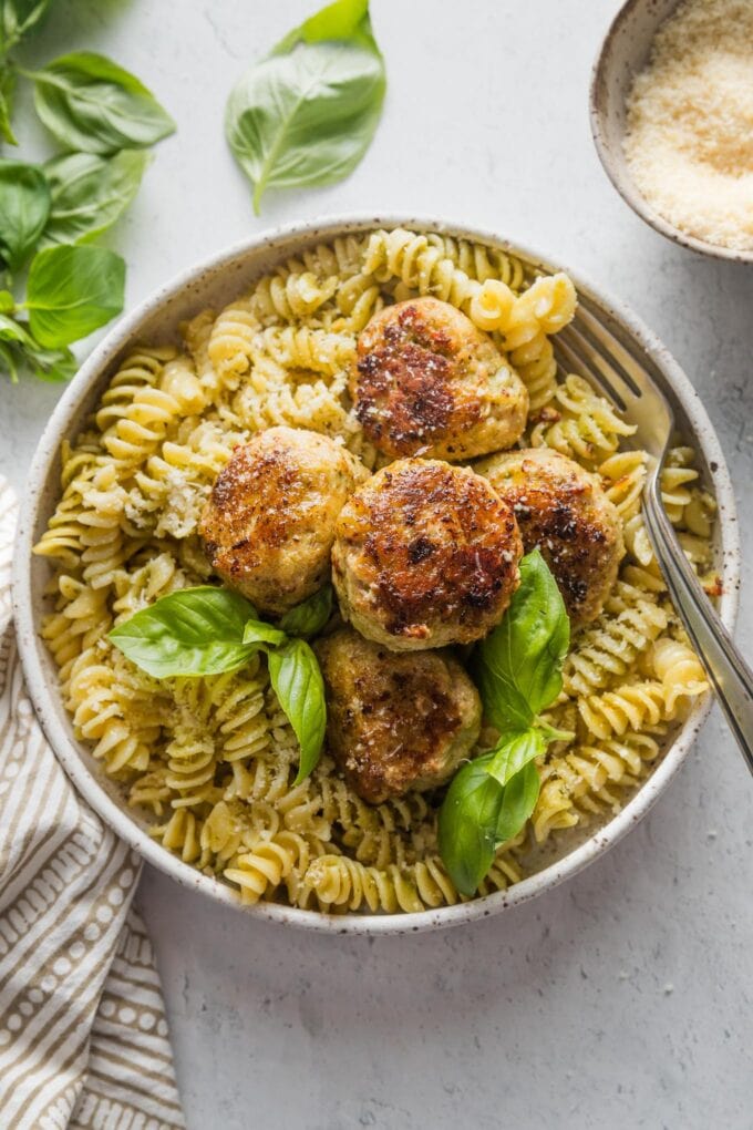 Ceramic bowl full of chicken pesto meatballs served over pasta.