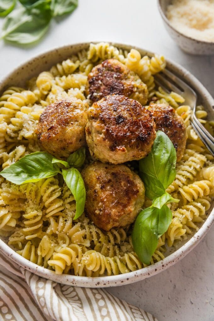 Close up of chicken pesto meatballs served over pasta with Parmesan and fresh basil.
