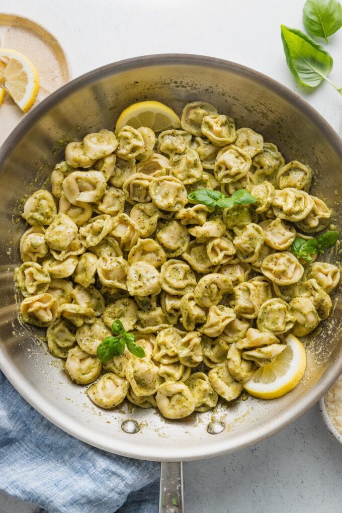 Skillet full of cheese tortellini in a light pesto cream sauce with lemon slices.