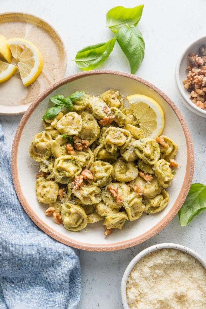 Low pasta bowl full of creamy pesto tortellini garnished with Parmesan and fresh basil leaves.