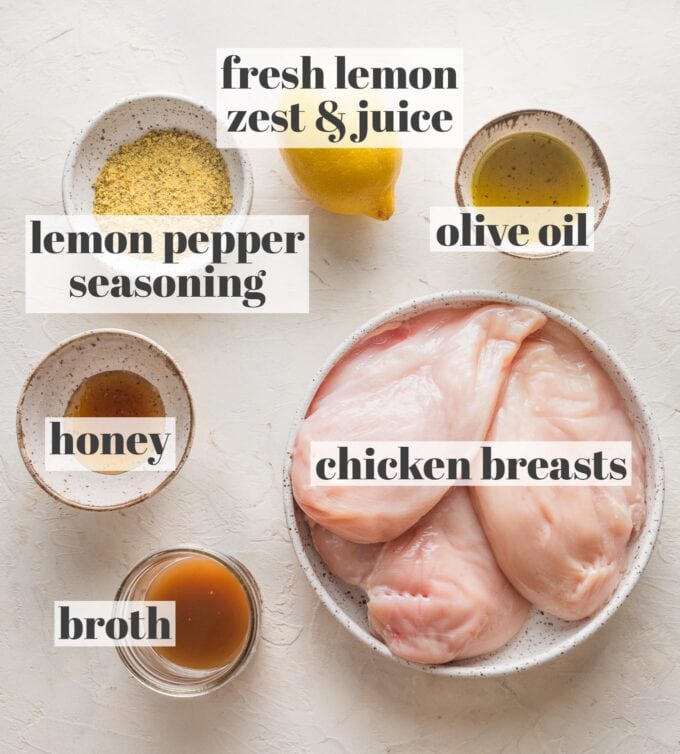 Labeled overhead image of chicken breasts, a lemon, olive oil, lemon pepper seasoning, honey, and chicken broth, all measured into prep bowls and ready to cook.