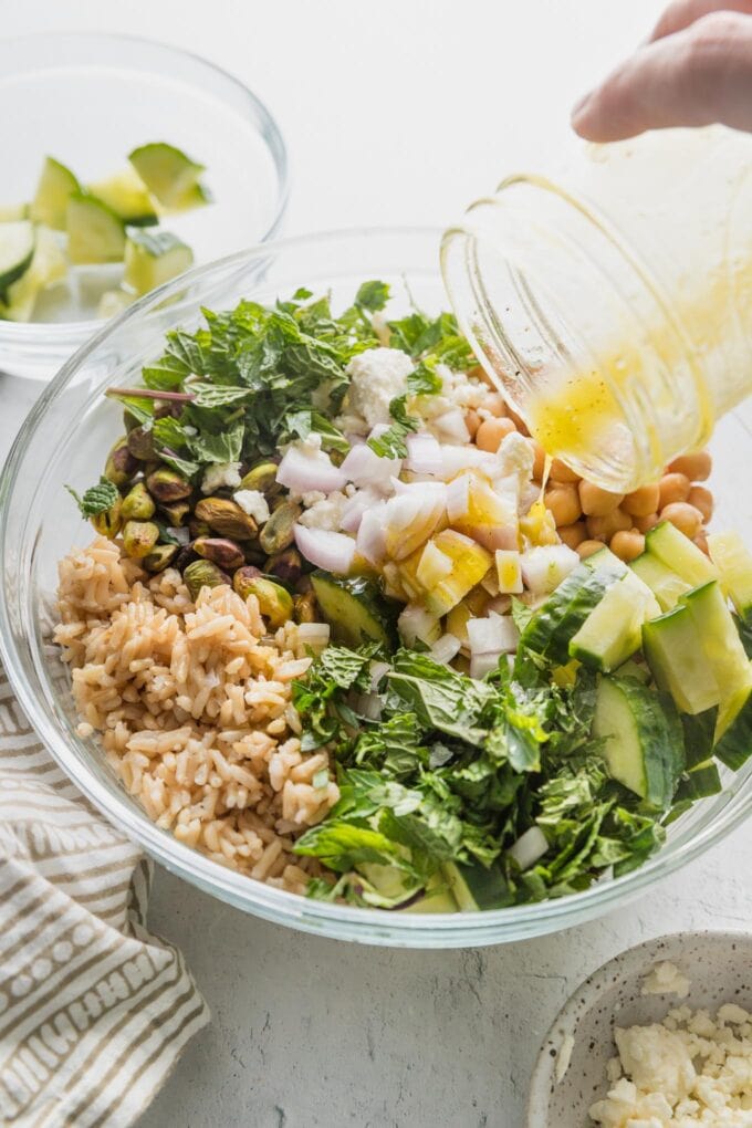 Small jar of olive oil lemon dressing being poured out on top of a salad.