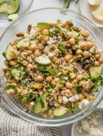 Clear glass prep bowl full of a Jennifer Aniston-style salad with brown rice, chickpeas, and herbs.