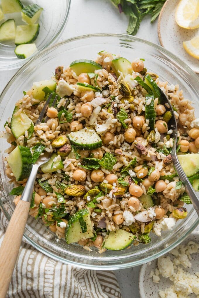 A fork and spoon tossing a large bowl full of Jennifer Aniston-style salad.