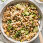 Low ceramic bowl full of a Jennifer Aniston-style salad made with brown rice, chickpeas, herbs, cucumbers, and shallot.