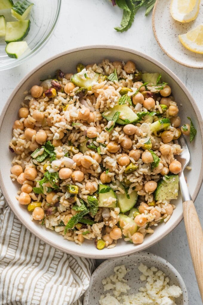 Low ceramic bowl full of a Jennifer Aniston-style salad made with brown rice, chickpeas, herbs, cucumbers, and shallot.