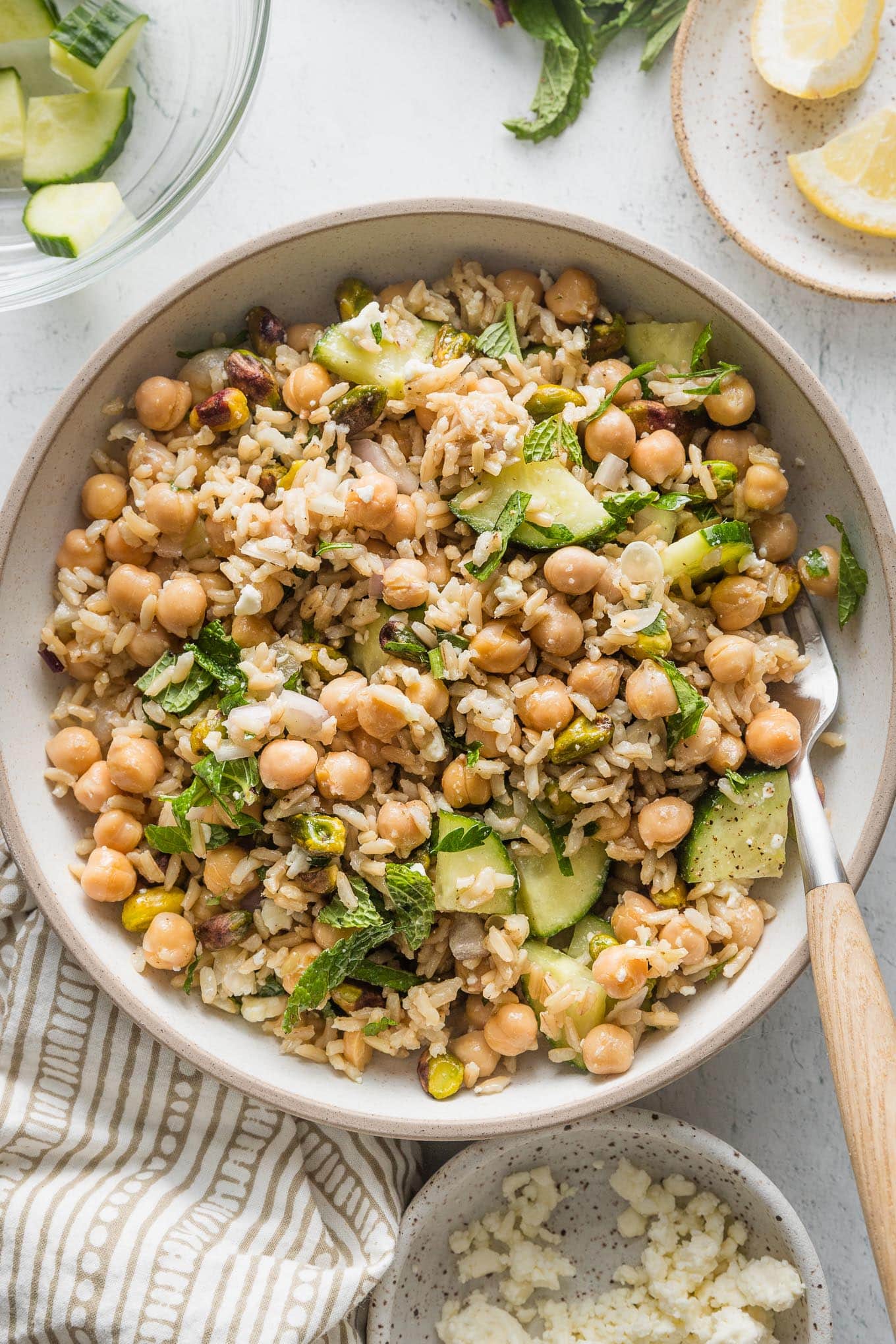 Low ceramic bowl full of a Jennifer Aniston-style salad made with brown rice, chickpeas, herbs, cucumbers, and shallot.