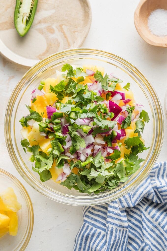Bowl full of pineapple, jalapeno, red onion, cilantro, lime juice, and salt, all ready to stir together into a fresh salsa.