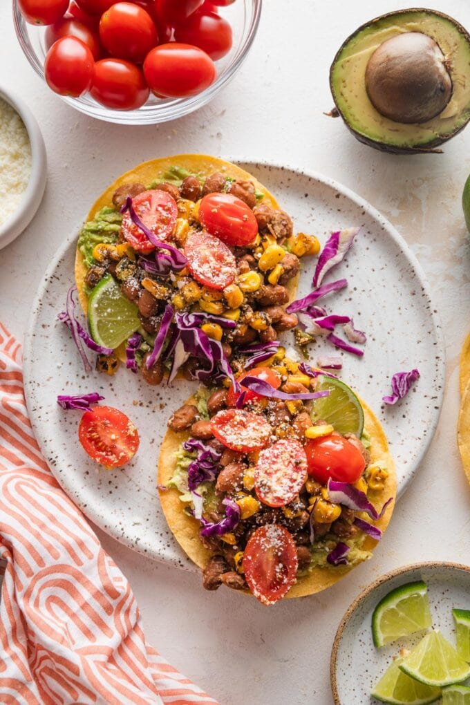 Countertop with a plate full of pinto bean tostadas, surrounded by extra salsa, tomatoes, avocado, and lime.