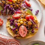 Small plate with a pinto bean tostada topped with a street corn tomato salsa, crumbled Cotija cheese, and shredded cabbage.