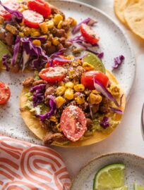 Small plate with a pinto bean tostada topped with a street corn tomato salsa, crumbled Cotija cheese, and shredded cabbage.