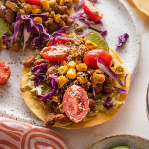 Small plate with a pinto bean tostada topped with a street corn tomato salsa, crumbled Cotija cheese, and shredded cabbage.
