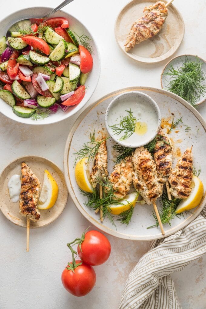 Countertop set with a large platter of chicken skewers and a side dish of cucumber tomato salad.