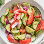 White bowl full of tomato cucumber salad with fresh dill and a red wine vinaigrette.