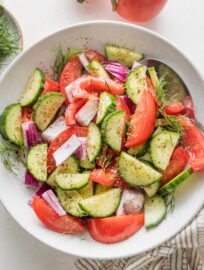 White bowl full of tomato cucumber salad with fresh dill and a red wine vinaigrette.