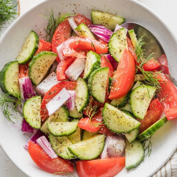 White bowl full of tomato cucumber salad with fresh dill and a red wine vinaigrette.