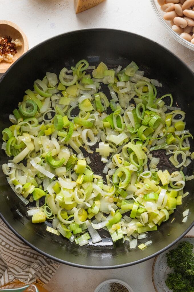 Leeks and yellow onions being sauteed together in a large cast iron skillet.