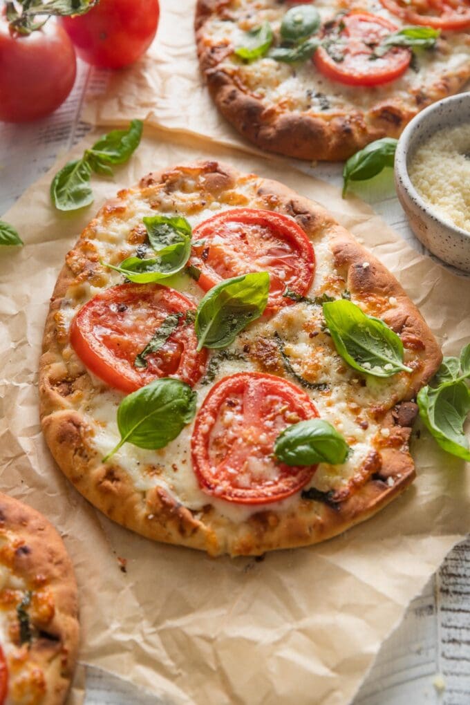 Angled view of a countertop with several naan flatbread pizzas made in a caprese style with mozzarella and tomatoes.