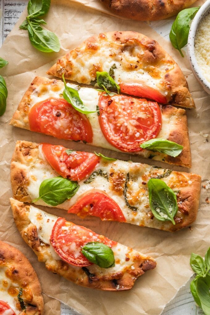Sliced caprese flatbreads scattered with lots of fresh basil leaves.