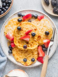 Overhead view of a plate of cottage cheese pancakes served with berries and maple syrup.
